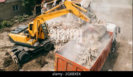 La pelle hydraulique brise les bâtiments et charge les déchets de construction dans le camion avec son godet. Démolition de bâtiments. Banque D'Images