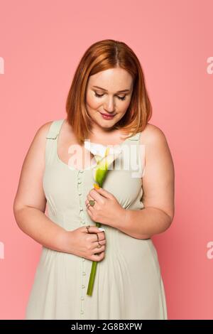 Femme aux cheveux rouges regardant la calla lys isolée sur rose Banque D'Images