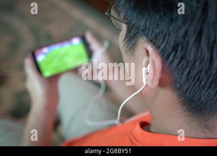 Homme regardant le football et le sport sur téléphone portable. Mise au point sélectionnée sur les écouteurs. Banque D'Images