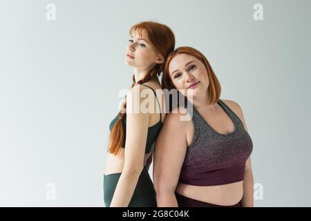 Taille plus et sportswomen à l'estime debout dos à dos isolé sur gris Banque D'Images