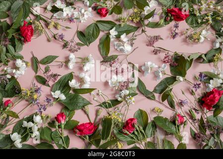 Arrangement floral avec différentes fleurs fraîches, feuilles et brindilles sur un fond rose. Banque D'Images