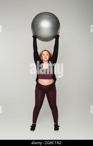 Femme de taille plus tenant le ballon de fitness sur fond gris