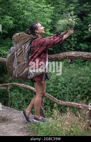 Attrayante fille touriste avec un grand sac à dos pour le voyage et avec un bouquet de fleurs sauvages. Banque D'Images