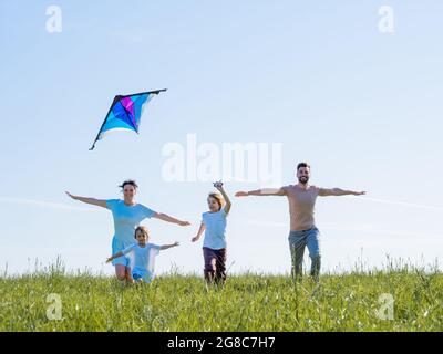 Parents et enfants courant avec cerf-volant pendant les vacances d'été, prairie parfaite et ciel en bord de mer Banque D'Images