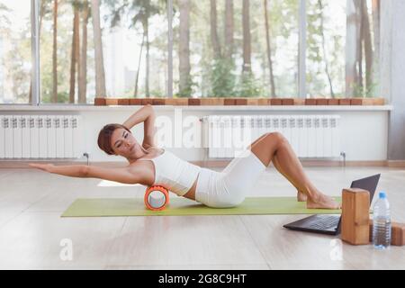 Femme sportive faisant des exercices en ligne avec rouleau en mousse sous le dos. Entraînez-vous en ligne avec un ordinateur portable. Formateur en ligne Banque D'Images