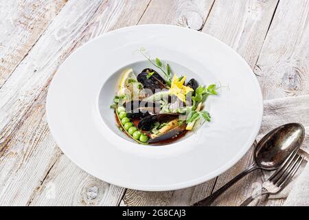 Moules aux pois verts et cornichons dans une sauce au vin sur une assiette blanche. Fruits de mer sains et délicieux. Recette de restaurant. Service avec serviette et couverts Banque D'Images