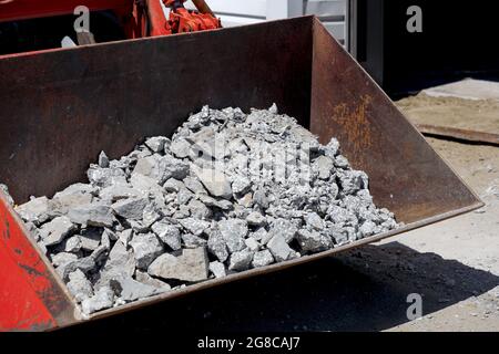 Élimination des débris de construction. Le godet du tracteur est rempli de débris de béton et de pavés. Démantèlement de la chaussée sur la rue. Banque D'Images