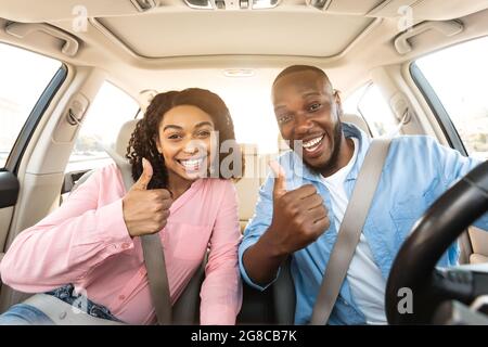 Heureux couple noir assis dans la voiture gestante pouces vers le haut Banque D'Images