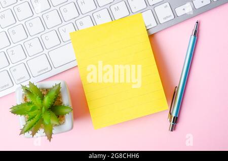 Le pense-bête jaune vierge sur le clavier de l'ordinateur pour votre texte ou message sur fond rose. Banque D'Images