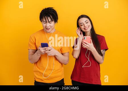 Jeune couple multiracial écoutant de la musique avec des écouteurs et des téléphones portables isolés sur un mur jaune Banque D'Images