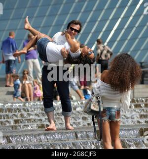 Homme tenant rire fille sur les mains se tenant parmi les jets d'eau de la fontaine, une autre fille prenant la photo d'eux. 21 juin 2019. Kiev, Ukraine Banque D'Images