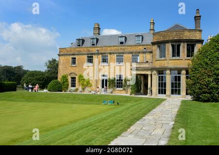 Les gens glamour s'assoient sur le patio en face d'une belle maison géorgienne appelée Maison Hadspen dans le Somerset. Il fait partie du nouvel hôtel Newt près de Bruton. Une pelouse de croquet repose au premier plan. L'image reflète une belle maison de campagne anglaise classique avec des gens qui l'apprécient au soleil. Banque D'Images