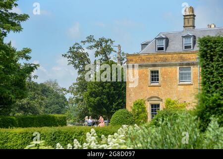 Les gens glamour s'assoient sur le patio en face d'une belle maison géorgienne appelée Maison Hadspen dans le Somerset. Il fait partie du nouvel hôtel Newt près de Bruton. Un jardin luxuriant se trouve au premier plan. L'image reflète une belle maison de campagne anglaise classique avec des gens qui l'apprécient au soleil. Banque D'Images