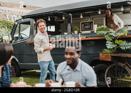 Homme parlant avec des amis près d'un camion alimentaire avec un vendeur Banque D'Images