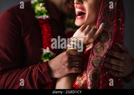 vue partielle d'un indien flou en turban tenant la main d'une mariée heureuse dans un foulard traditionnel isolé sur le gris Banque D'Images