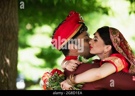 Un Indien en turban embrassant une jolie mariée dans un foulard traditionnel Banque D'Images