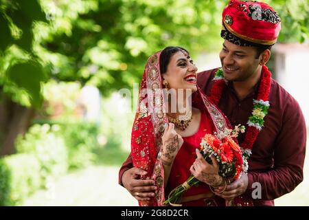 couple indien heureux marié dans des vêtements de mariage traditionnels regardant l'un l'autre à l'extérieur Banque D'Images