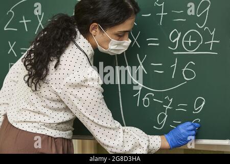 Enseignante portant un masque facial avec des gants en latex et expliquant une formule mathématique à la classe Banque D'Images