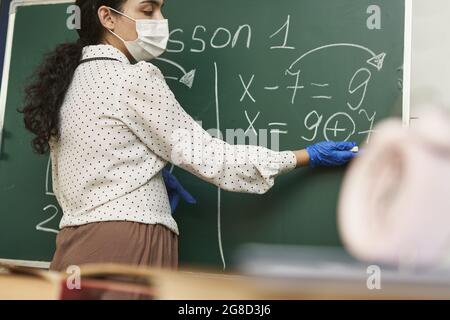 Enseignante portant un masque facial avec des gants en latex et expliquant une formule mathématique à la classe Banque D'Images