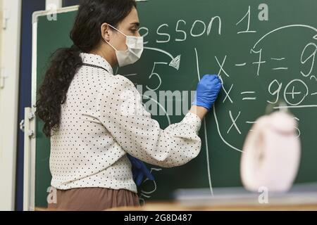 Enseignante portant un masque facial avec des gants en latex et enseignant une formule mathématique à la classe Banque D'Images