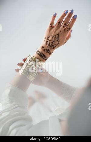 vue partielle de la femme indienne avec mehndi portant un bracelet doré tout en se préparer à un mariage sur blanc Banque D'Images
