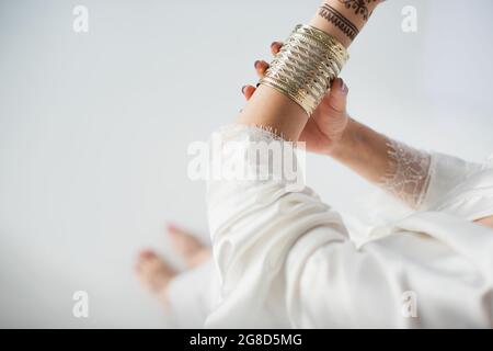 vue partielle d'une femme indienne avec des mehndi sur les mains portant un bracelet doré tout en se préparer à un mariage sur blanc Banque D'Images