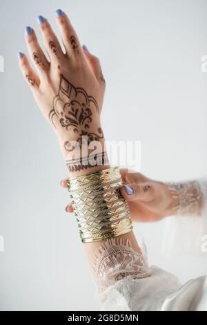 vue rognée d'une femme indienne avec des mehndi sur les mains portant un bracelet doré tout en se préparer à un mariage isolé sur blanc Banque D'Images