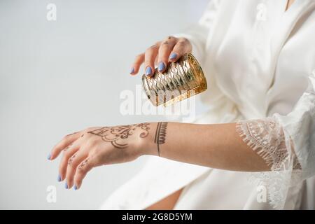 vue courte d'une femme indienne avec mehndi à la main portant un bracelet tout en se préparer à un mariage isolé sur blanc Banque D'Images