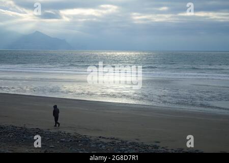 Dinas Dinlle Beach, Caernarfon, au nord du pays de Galles.Paysage d'hiver avec vue sur la côte et la mer.Une personne solitaire marche sur le sable. Banque D'Images