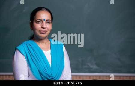 Portrait d'un professeur indien confiant debout devant le tableau noir dans la salle de classe Banque D'Images