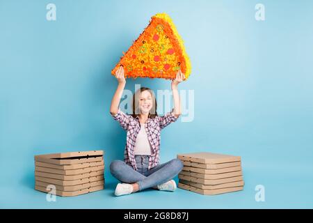 Portrait pleine longueur de drôle de jeune fille s'asseoir les mains tenir la grande pizza au-dessus de la tête isolée sur fond bleu de couleur Banque D'Images