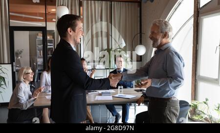 Joyeux chef d'équipe homme âgé qui donne la poignée de main à un employé enthousiaste Banque D'Images