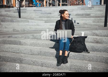 Une dame pleine d'esprit avec un gadget sur ses genoux, regardant loin Banque D'Images