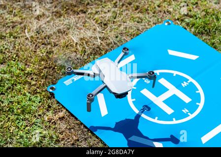 Le drone survole la zone d'atterrissage bleue de l'herbe, les hélices en plastique sont en marche et la caméra de la nacelle est visible. Banque D'Images