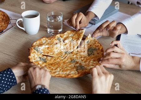 Pizza chaude sur la table de bureau, mains des employés prenant des tranches Banque D'Images
