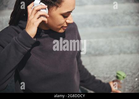 Une dame calme écoute la musique préférée assise sur les marches en béton Banque D'Images