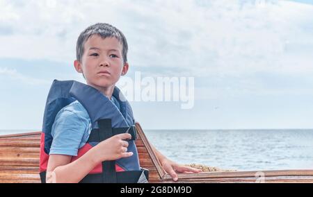 Penser asiatique garçon dans le gilet de sauvetage sur fond de mer et de ciel. Banque D'Images