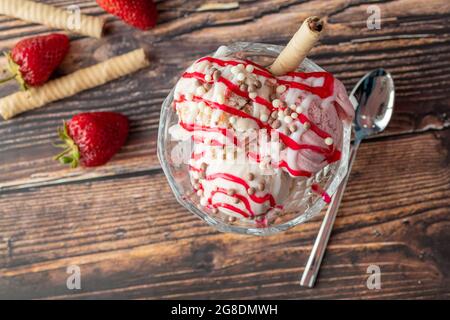 Crème glacée Roma à la fraise, à la banane et à la crème dans un bol en verre avec sauce rouge versée dessus. Banque D'Images