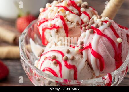 Crème glacée Roma à la fraise, à la banane et à la crème dans un bol en verre avec sauce rouge versée dessus. Banque D'Images