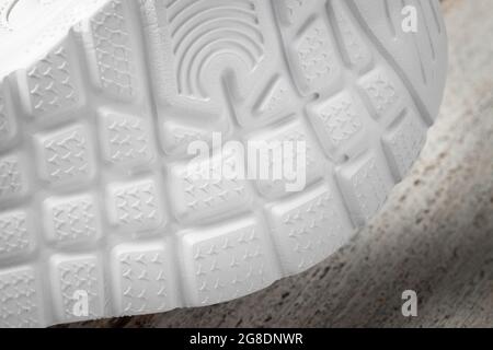 Macro photographie des semelles des sneakers blanches. Baskets de sport pour enfants couchés sur le côté avec semelle antidérapante en caoutchouc blanc sur un bois Banque D'Images