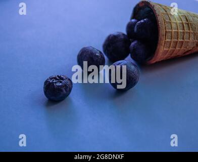 cornet de gaufres avec crème glacée et bleuets sur fond bleu. La crème glacée est isolée en gros plan. Banque D'Images