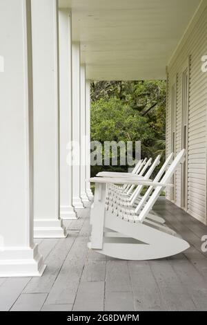 Une rangée de fauteuils à bascule blancs de style Adirondack, alignés sur un porche avec des piliers blancs. Wesley House, Eden Gardens, Floride, États-Unis Banque D'Images
