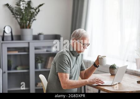 Portrait de l'homme moderne senior avec un ordinateur portable à la maison et un café, un espace de copie Banque D'Images