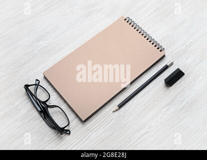 Ensemble de papeterie vierge. Livre de croquis, lunettes, crayon et gomme Kraft sur fond en bois clair. Modèle pour placer votre conception. MOC de conception réactive Banque D'Images