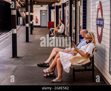 Un couple assis sur un banc sur la plate-forme attendant un train souterrain dans le centre de Londres portant des masques Banque D'Images
