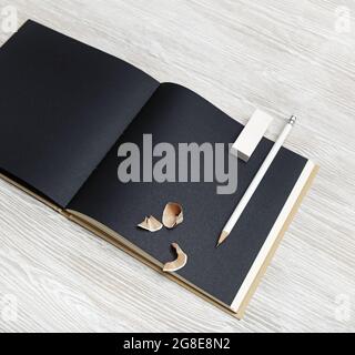 Photo d'un carnet noir vierge, d'un crayon et d'une gomme sur fond en bois clair. Banque D'Images