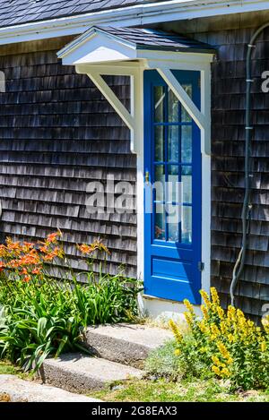 Une charmante porte bleue et un auvent à pignons sur une maison à galets accueille les randonneurs le long de la route principale sur l'île Mohegan, Maine. Copier l'espace. Banque D'Images