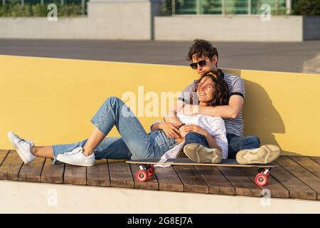 Un jeune couple amoureux s'assoit au coucher du soleil sur une longue planche. Homme et femme tendance qui se rafraîchvent en plein air Banque D'Images