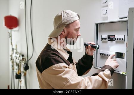 Un jeune électricien vérifie les interrupteurs du panneau de tension pendant le travail Banque D'Images