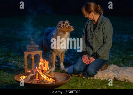 Le chien est assis près du feu de camp avec son propriétaire. La femme regarde avec amour le Berger allemand. Vacances en hiver, feu de bougie dans lanterne Banque D'Images